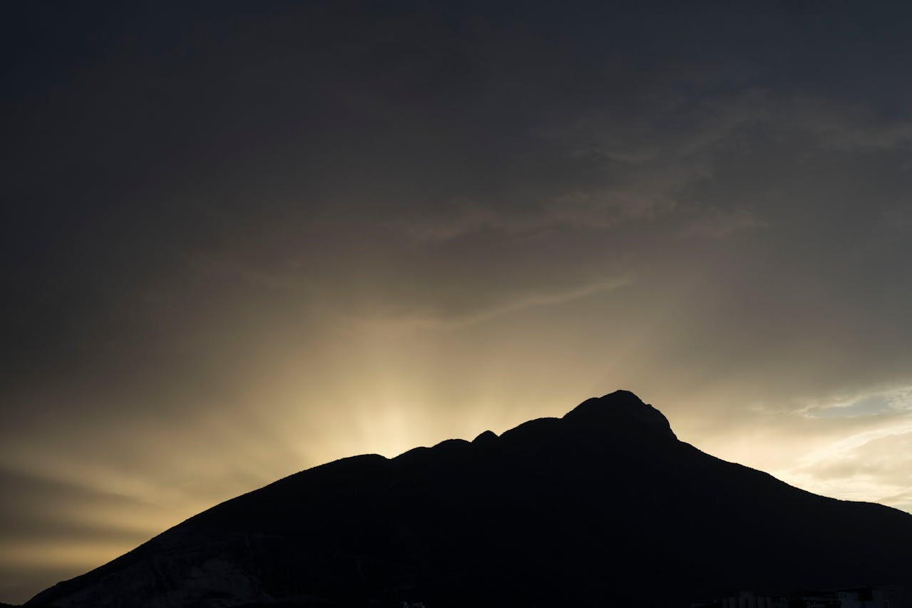 gallery-01 Dramatic sunset behind Cerro de la Silla, Monterrey, Mexico, casting striking silhouettes and sun rays.