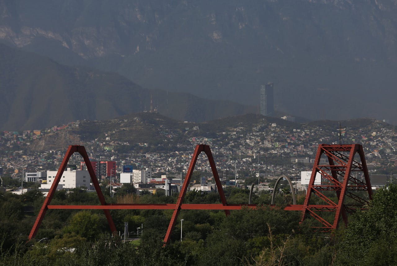 about-img-01 Red steel bridge with Monterrey cityscape and mountains in the background during daytime.